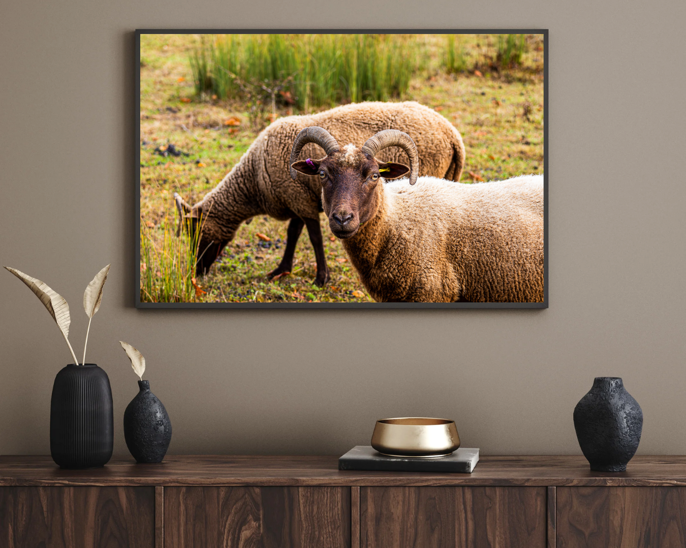 Framed picture of two rams on a wall above a wooden console table with decorative items.